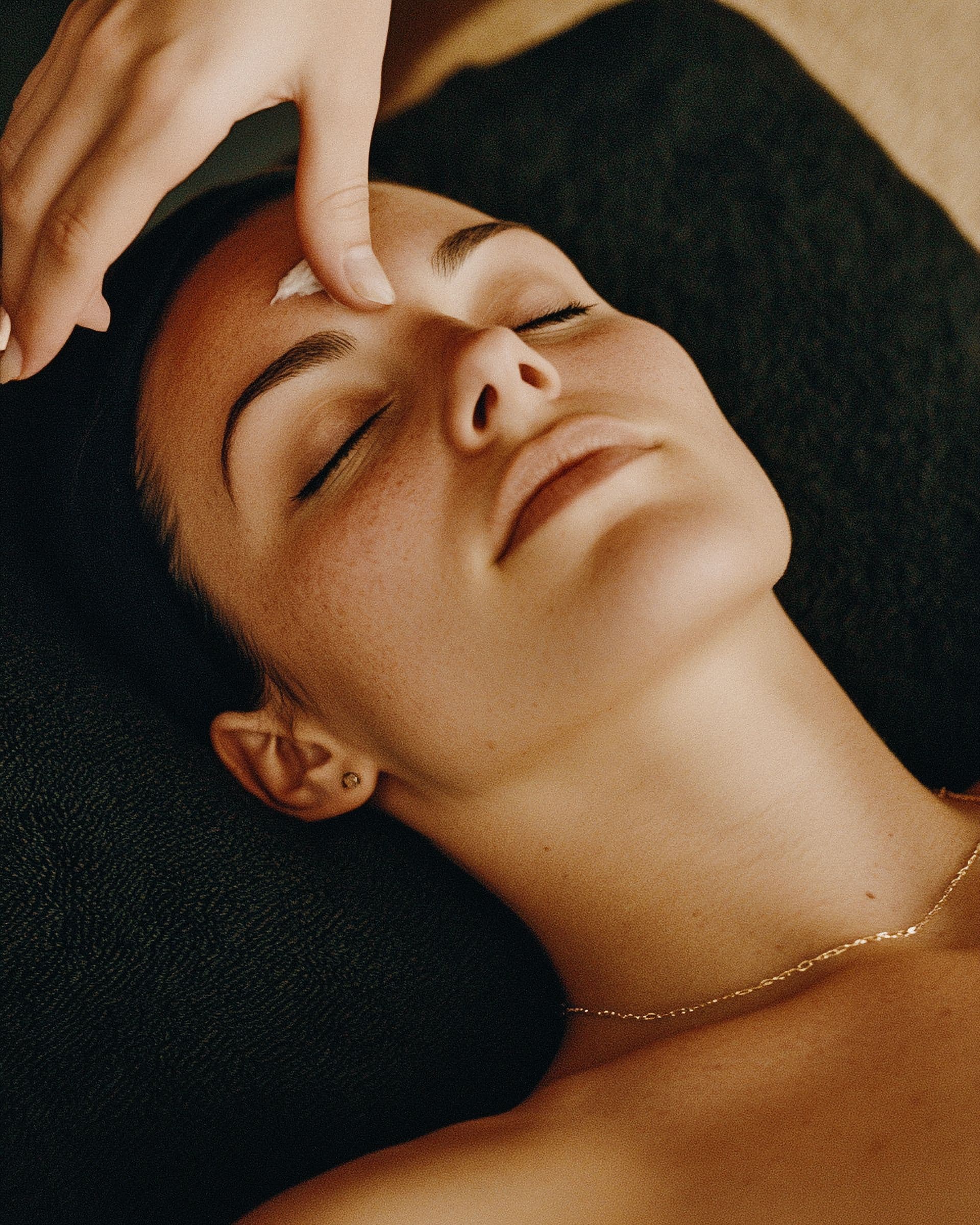 A woman relaxing with her eyes closed during a calming facial in warm light.