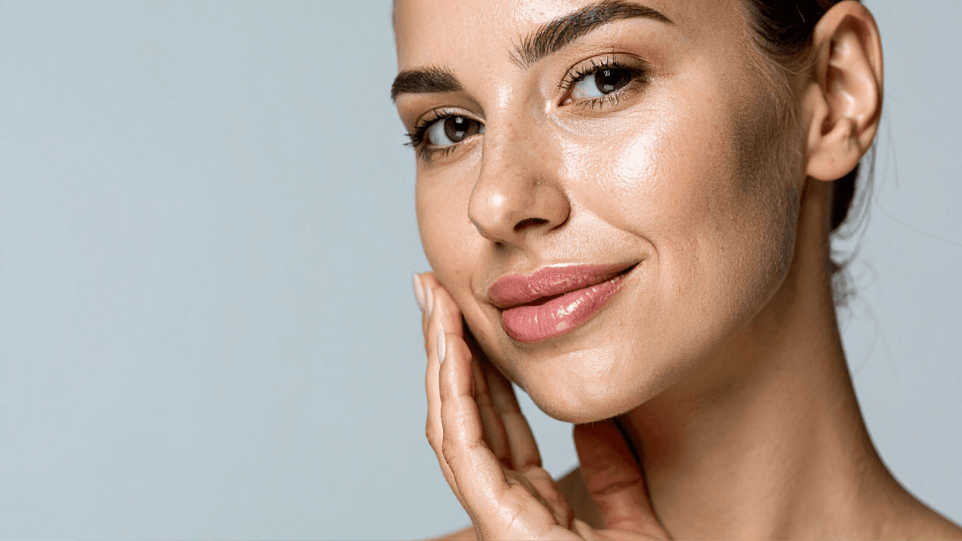 A close-up of luminous, dewy skin with a hand resting softly at the cheek.