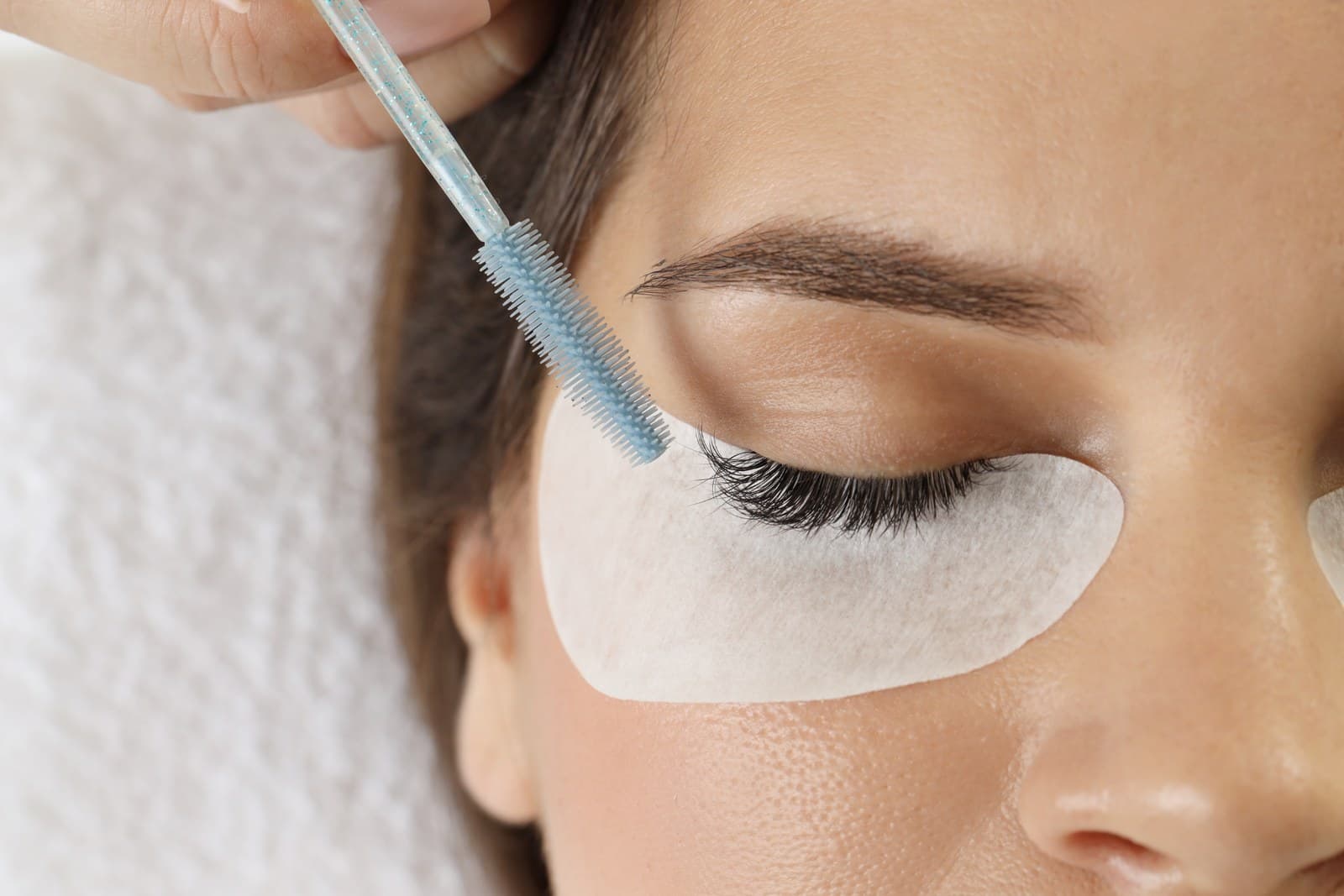 Close-up of a lash tint being applied with a wand over an under-eye gel patch.