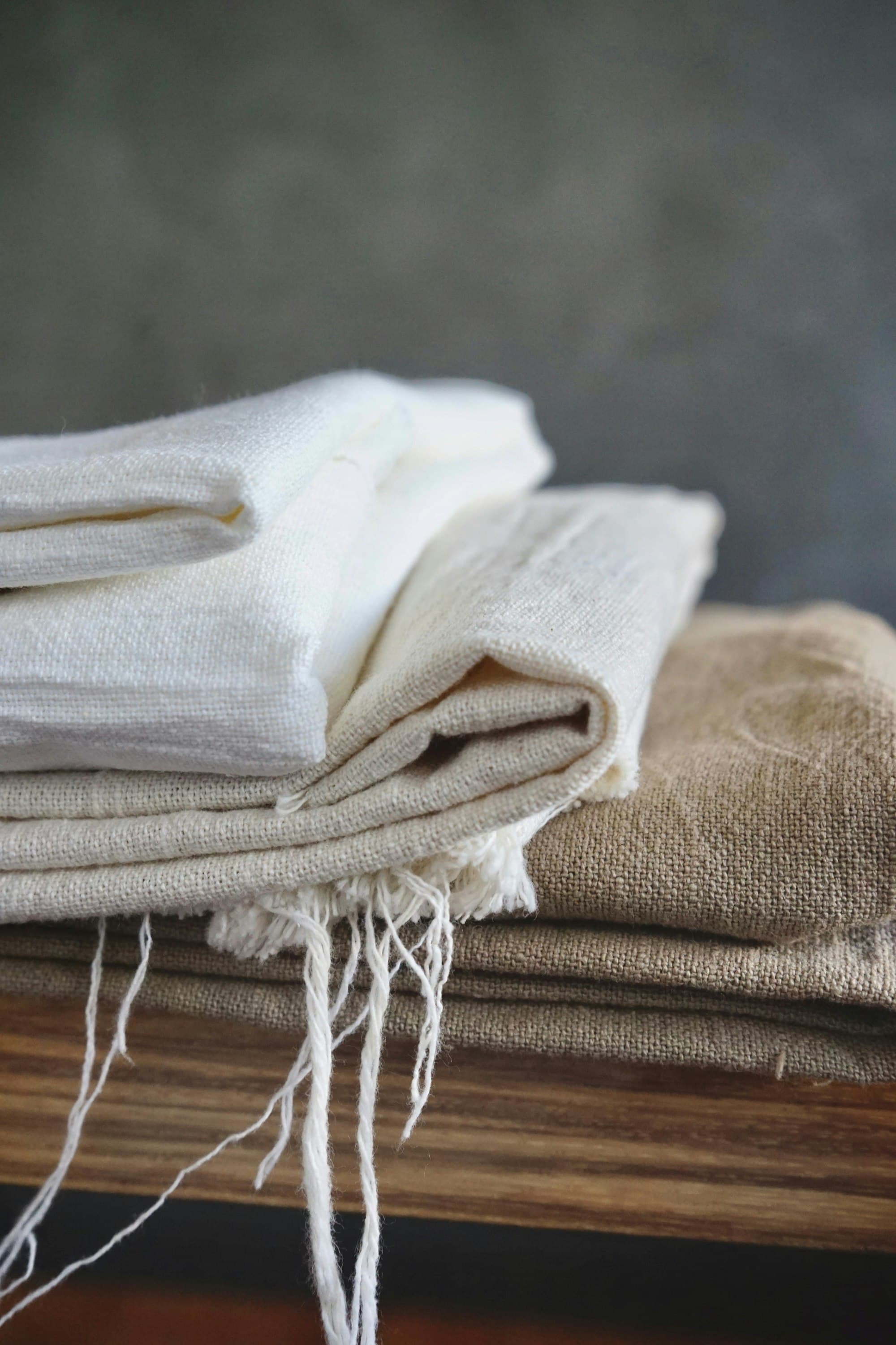 Soft white linen draped over a warm wooden surface in pooling natural light.