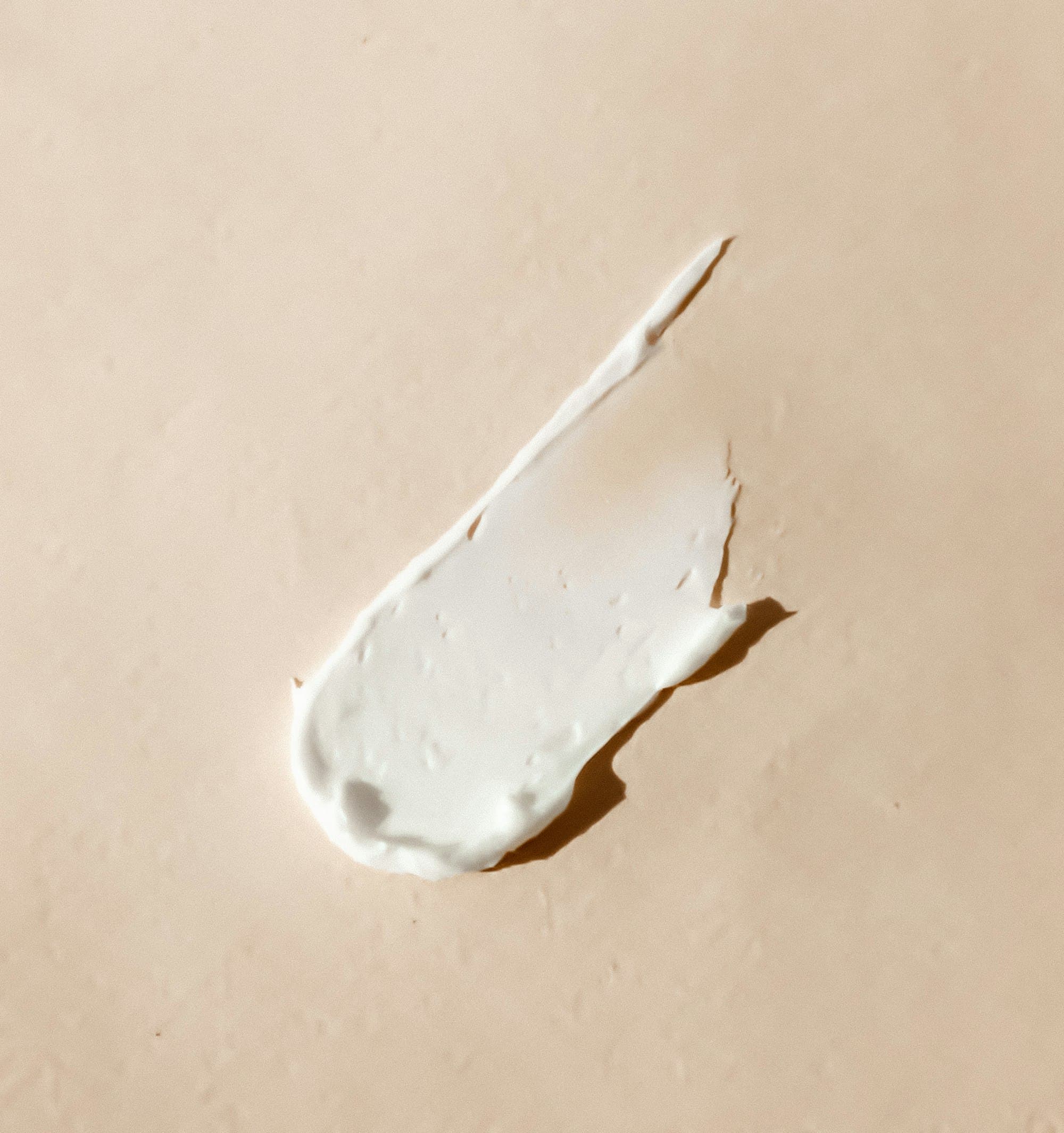 Macro close-up of a soft cream skincare smear swept across a warm beige surface.