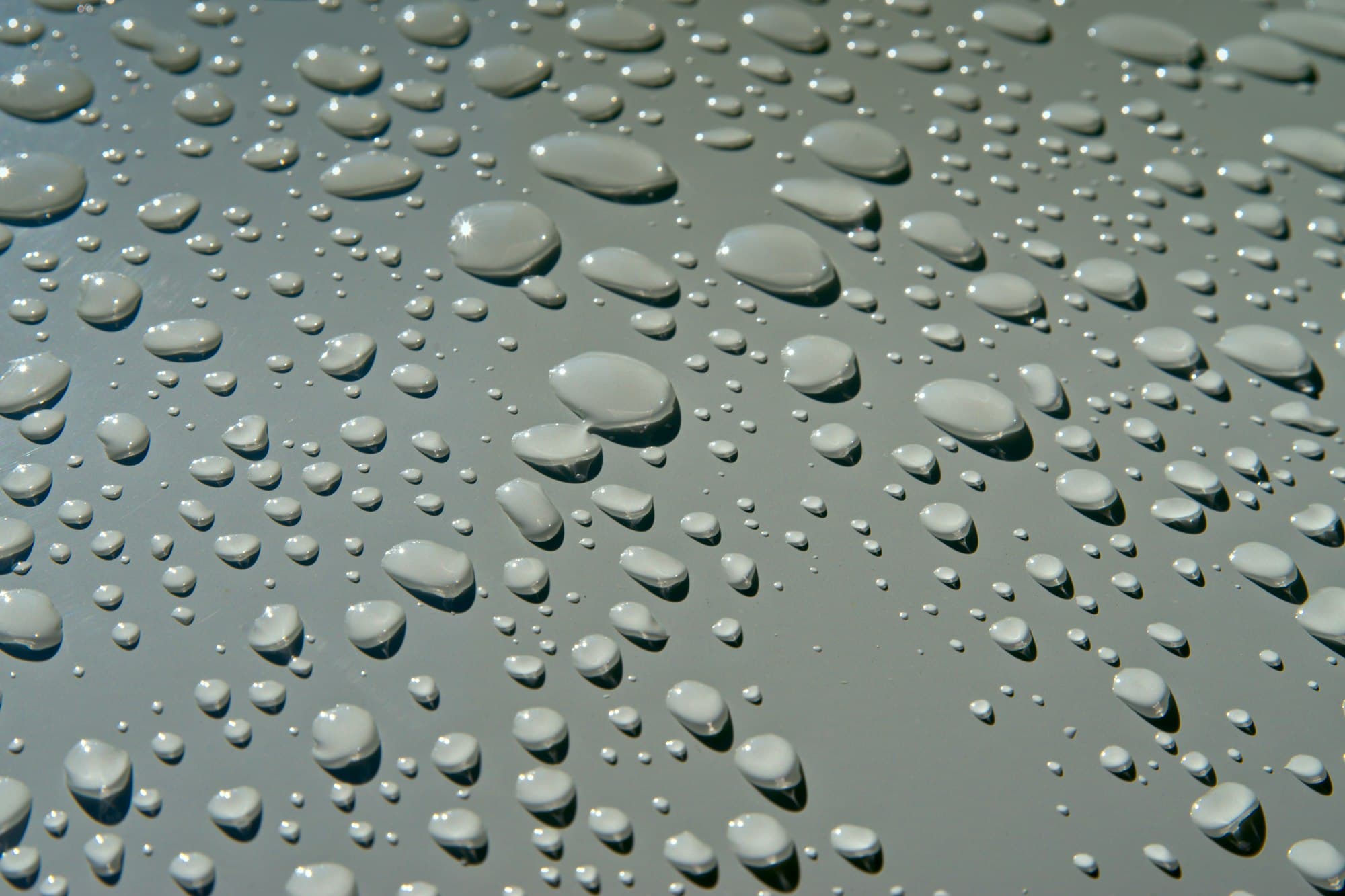 Close-up of fresh water droplets beaded on a smooth neutral surface, catching the light.